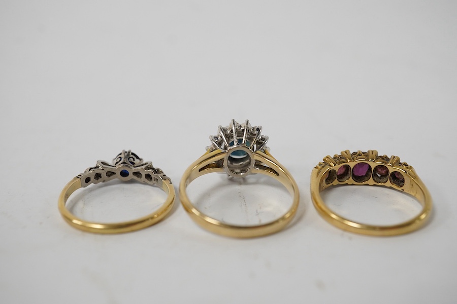 A group of three rings, comprising: a sapphire and diamond cluster ring, size M1/2, stamped 14K and 585; a five-stone ring set with cushion-shaped garnets and rose-cut diamonds, size L; and a synthetic sapphire and simul